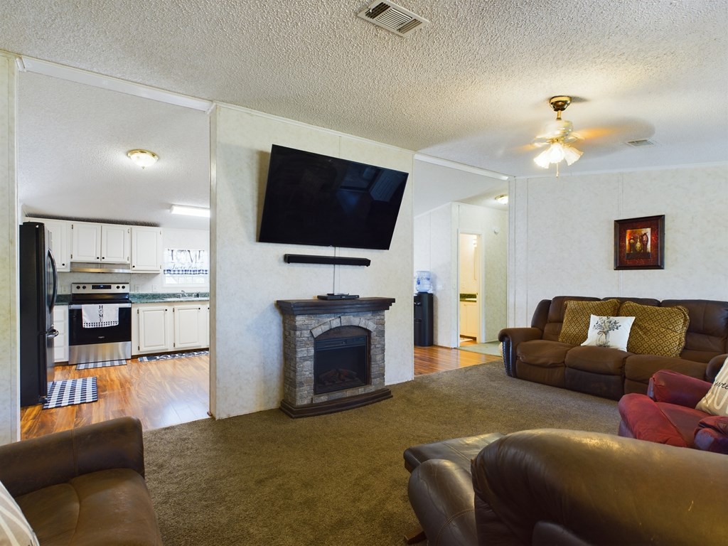 Living room with a stone fireplace and leather seating, open to a white-cabinet kitchen.