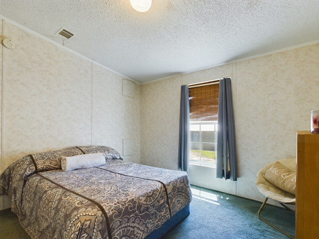 Bedroom with a patterned double bed, bamboo window shade, blue curtains, and blue carpet.
