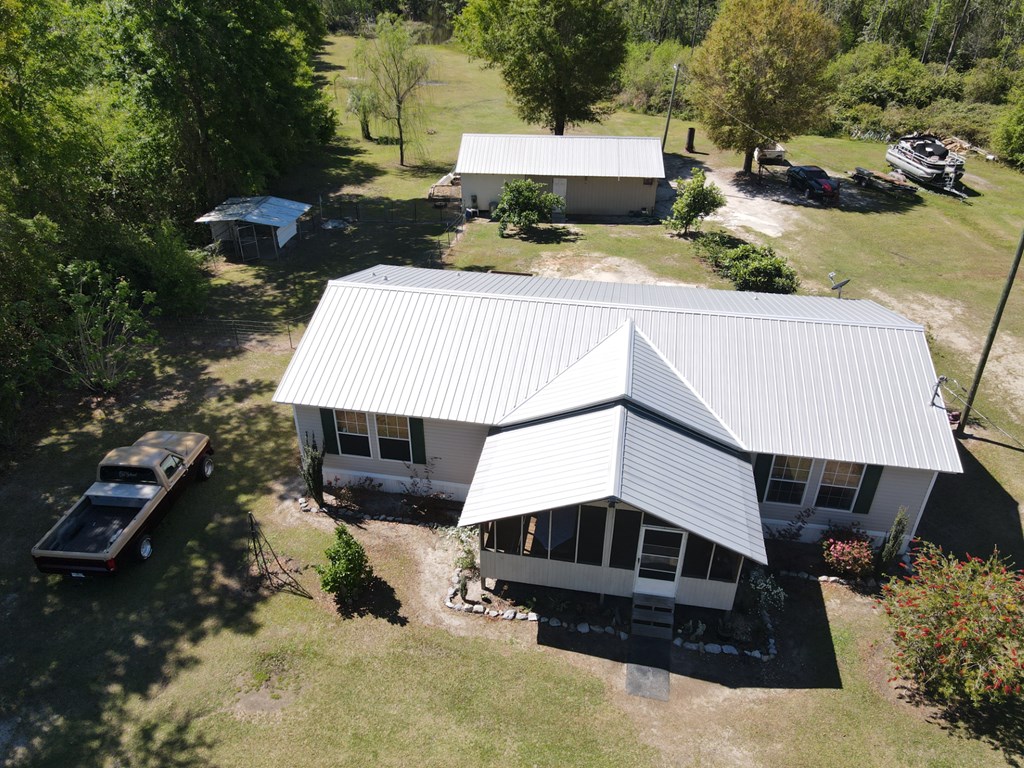 Aerial view of a light-roofed home, detached outbuilding, pickup truck, and boat on a spacious rural lot.