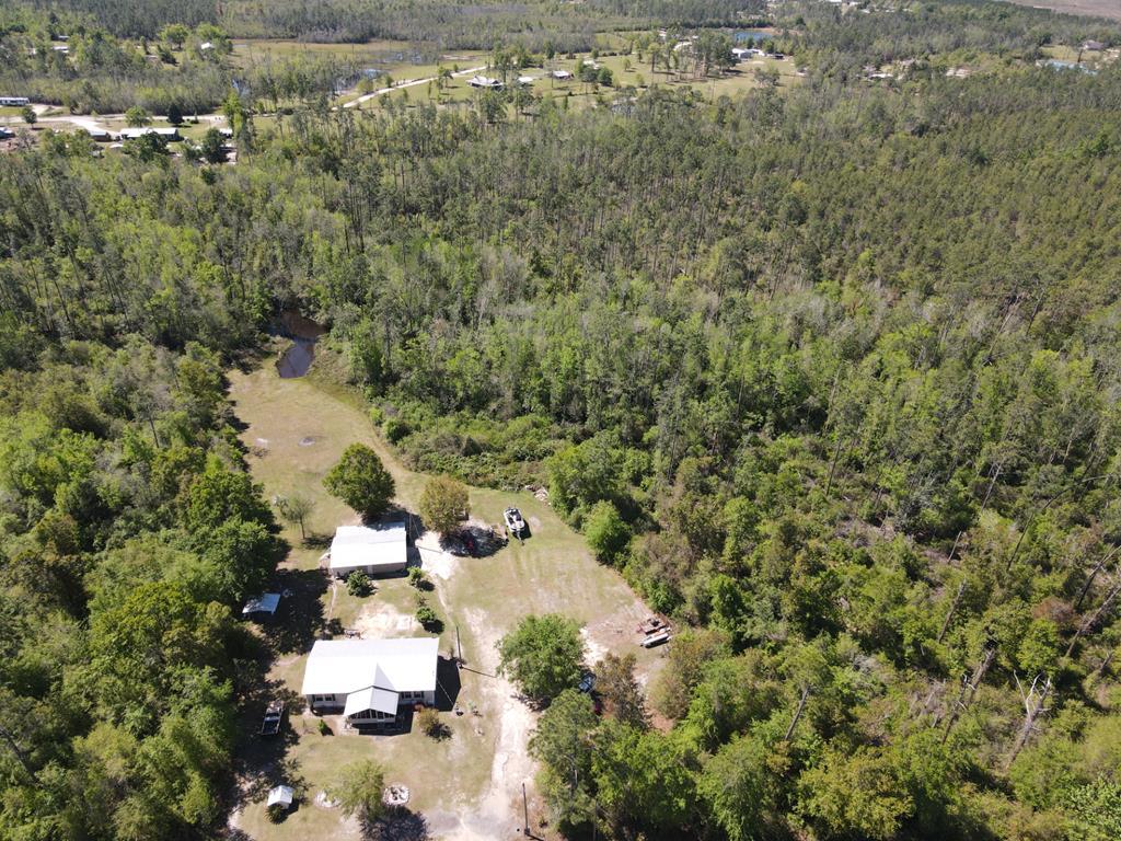 Aerial view of a wooded rural property with a house, outbuildings, grassy clearing, and small pond.