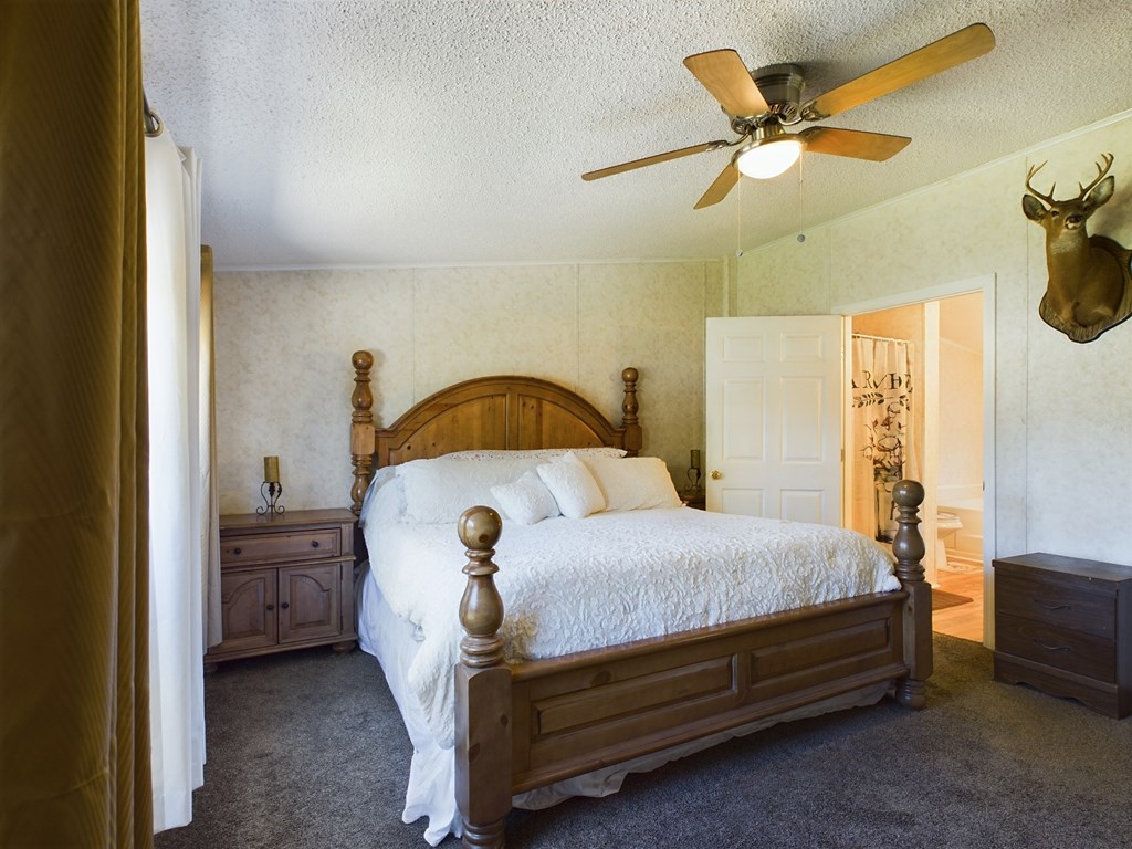 Bedroom with a dark wood four-poster bed, white bedding, ceiling fan, and mounted deer head.