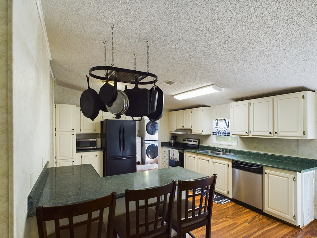 Kitchen with cream cabinets, green countertops, hanging pots, and a peninsula with dining chairs.