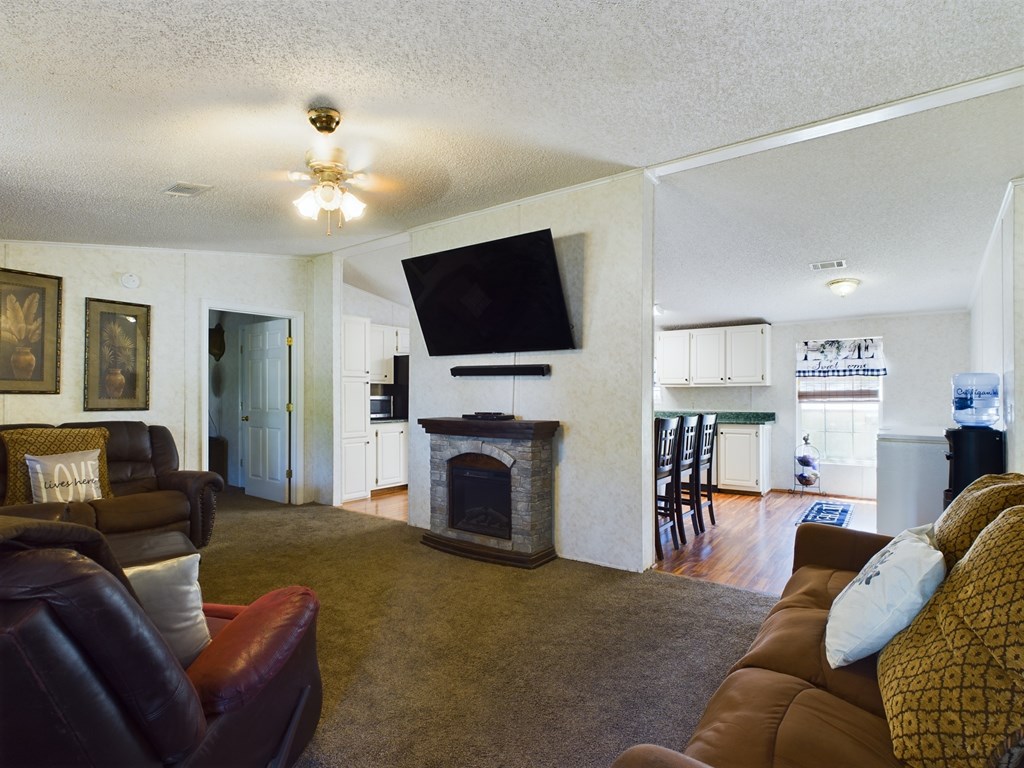 Living room with leather seating and stone fireplace, open to a bright kitchen and dining area.