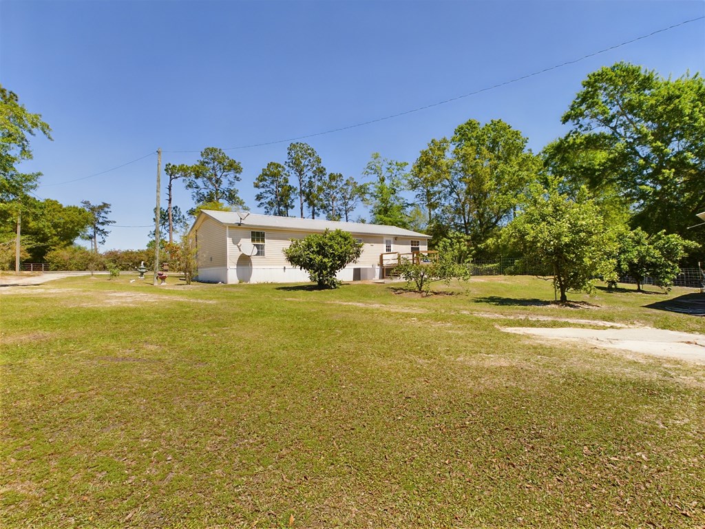 Single-story light-sided home with a metal roof, set in a broad grassy yard.