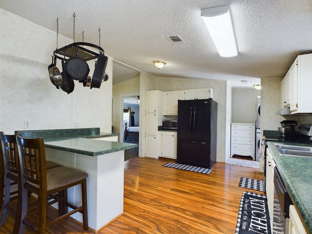 Kitchen with green countertops, white cabinets, a black refrigerator, and a peninsula with bar seating.