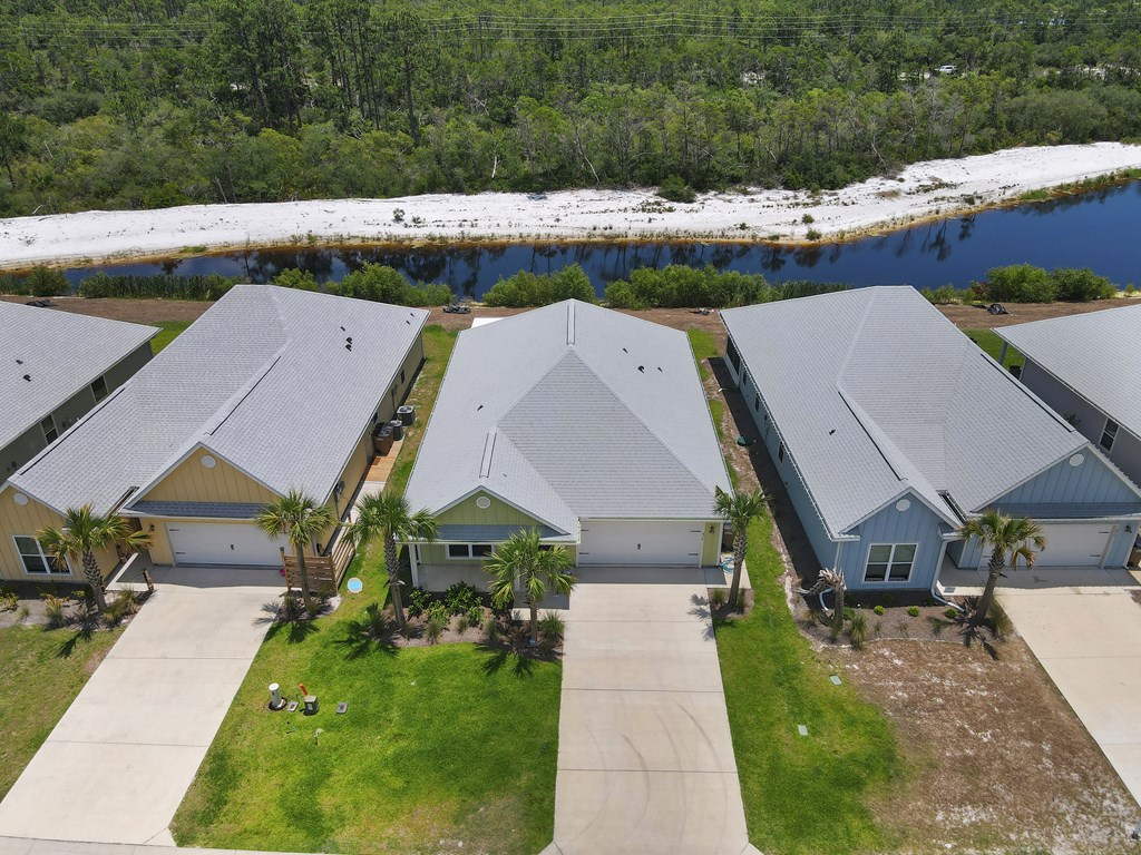 Aerial view of homes beside a waterway, with a sandy wooded shoreline beyond.