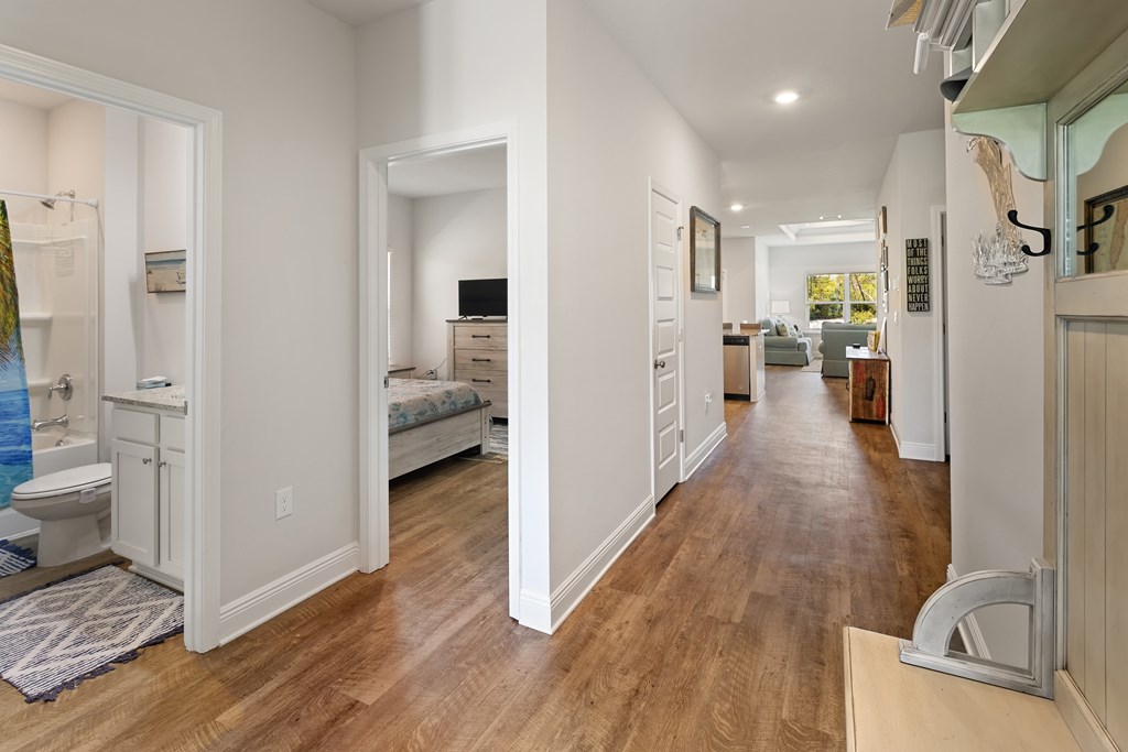 Hallway with wood-look flooring, a bathroom and bedroom doorway, and the living area beyond.