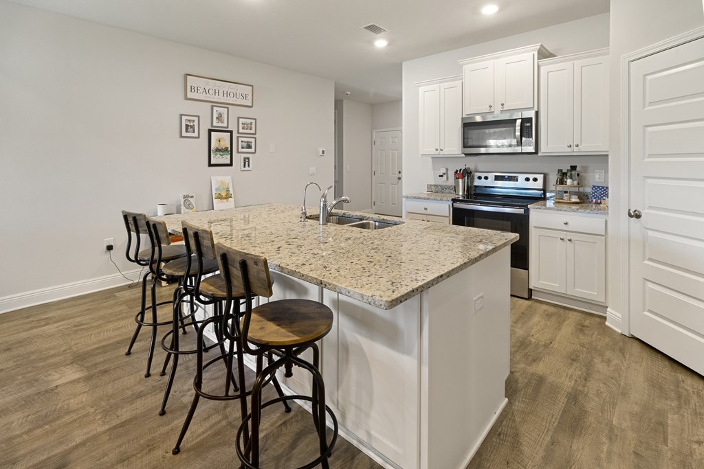 Kitchen with a large stone island, four bar stools, white cabinets, and stainless steel appliances.
