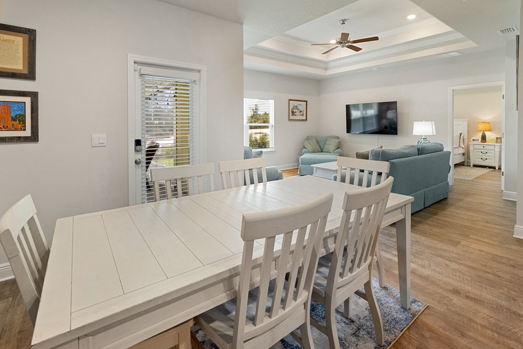 Dining area with a white table and chairs overlooking a living room with blue sofas and a tray ceiling.