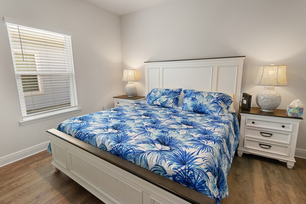 Bedroom with a white bed, blue palm-print bedding, matching nightstands, and window blinds.