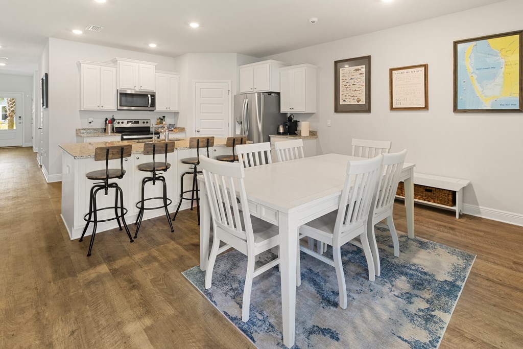 Open-plan kitchen and dining area with white cabinetry, island bar stools, and a dining table on a blue rug.