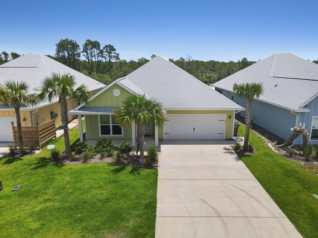 Single-story green house with a two-car garage, wide driveway, and palm trees.