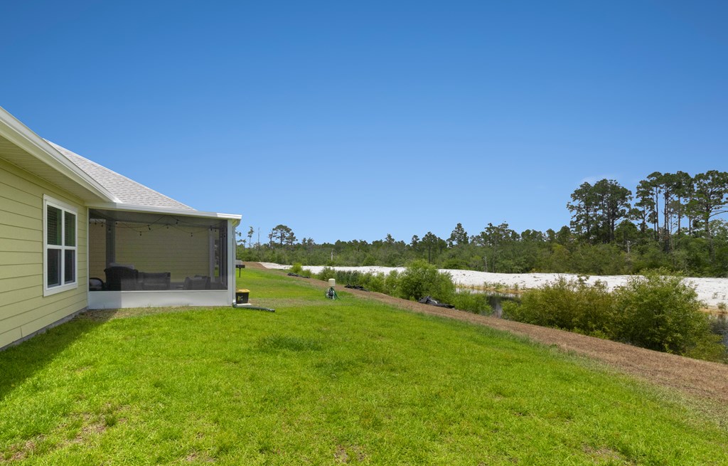 Backyard with a broad green lawn, covered screened patio, and sandy ground beyond.