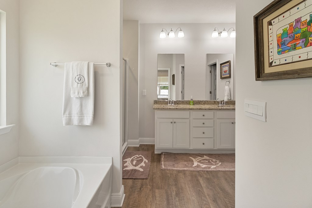 Bathroom with a white bathtub, double vanity, stone countertop, and turtle-pattern bath mats.