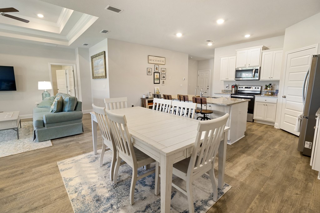 Open-plan dining room and kitchen with white farmhouse table, granite island, and adjoining living area.