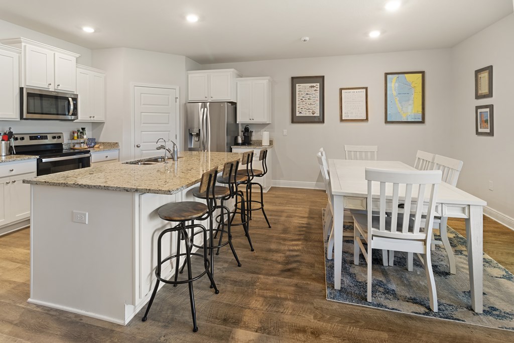 Open-plan kitchen and dining area with a granite island, stainless steel appliances, and white dining furniture.