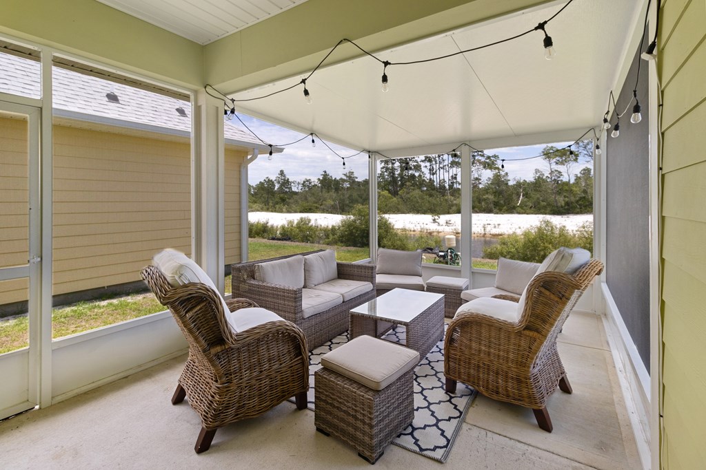 Screened porch with wicker seating and string lights overlooking sand and trees.