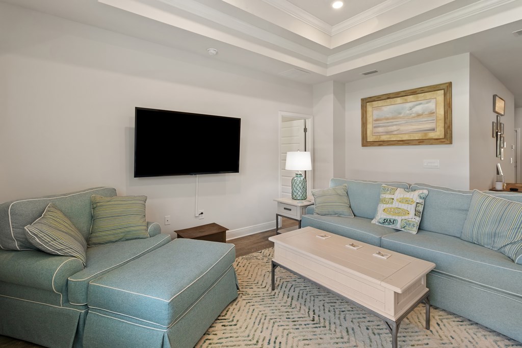 Living room with blue-green sofas, a white coffee table, patterned rug, and wall-mounted television.
