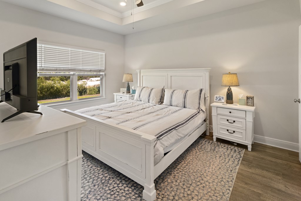 Bedroom with a white paneled bed, striped bedding, matching nightstands, and a window overlooking greenery.