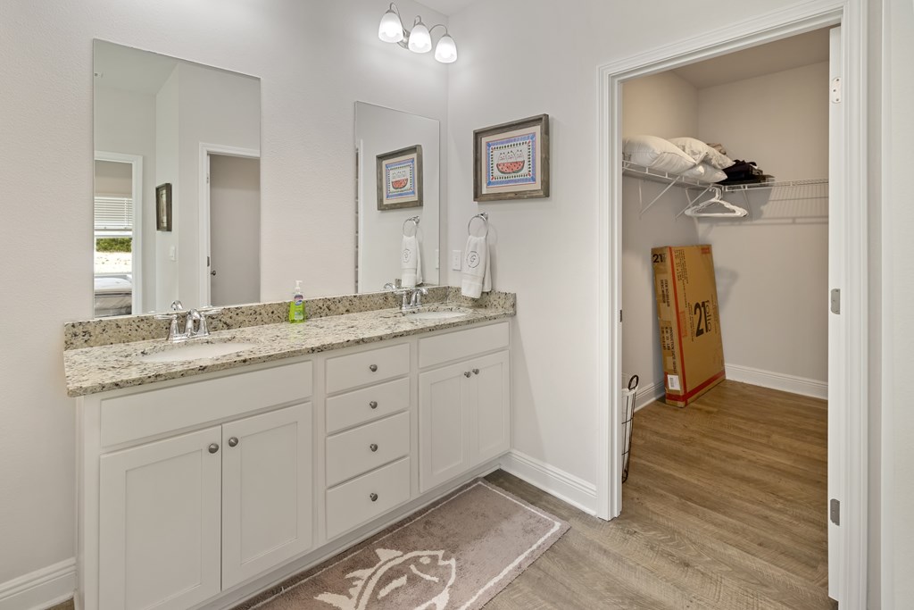 Bathroom with double-sink vanity, stone countertop, and an open closet.