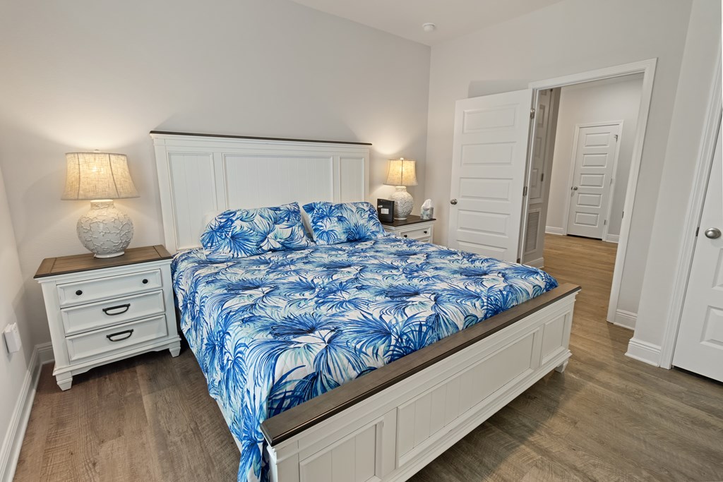 Bedroom with a white paneled bed, blue tropical-leaf bedding, matching nightstands, and an open doorway.