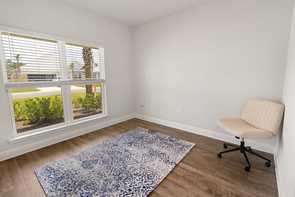Bright room with wide windows, a blue patterned rug, and a cream swivel chair.