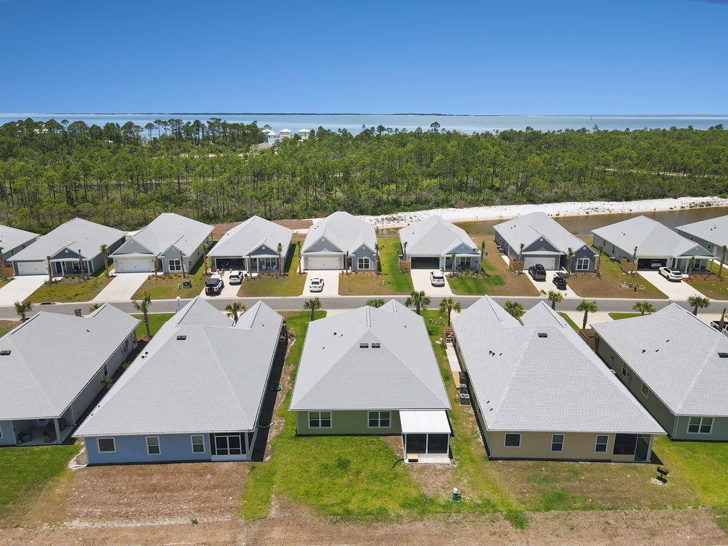 Aerial view of coastal homes with a wooded shoreline and water in the distance.