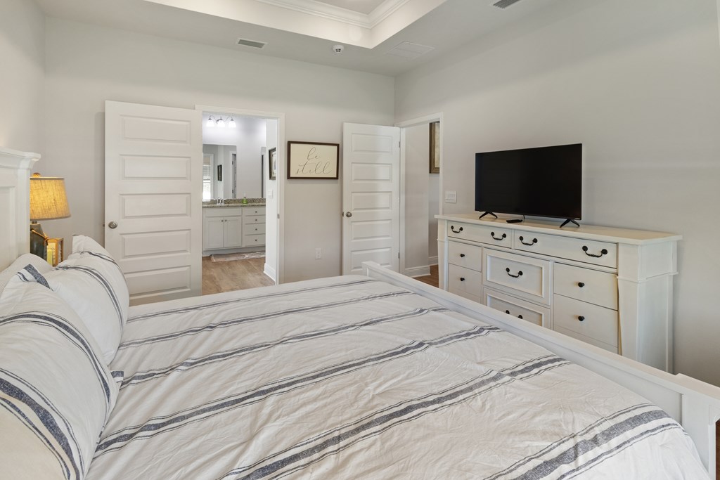 Bedroom with striped white bedding, a white dresser and TV, and an open doorway to the bathroom.