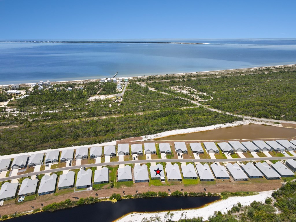 Aerial view of coastal homes beside wooded land and blue water, with one home marked by a red star.