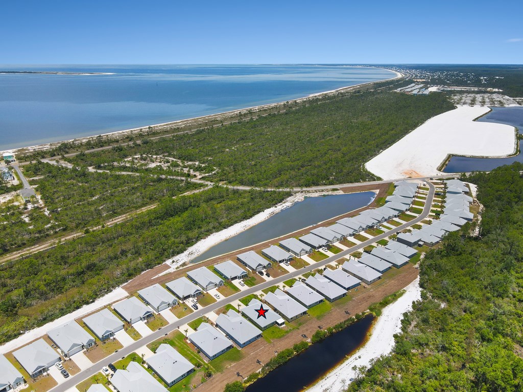 Aerial view of the marked home in a coastal neighborhood beside a bay and wetlands.