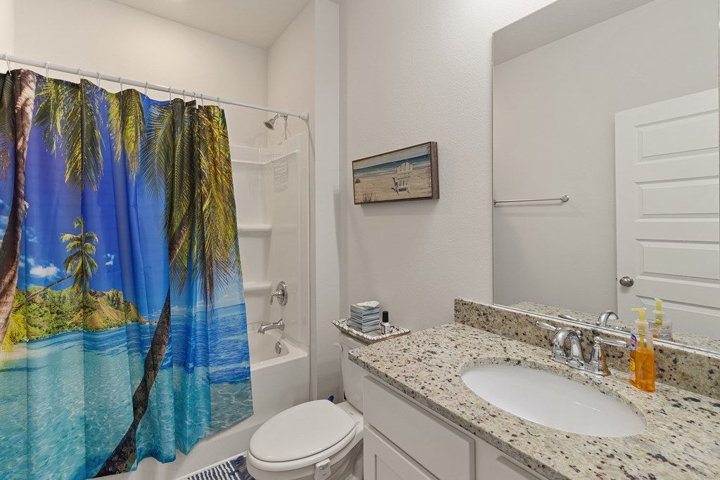 Bathroom with granite vanity and tropical beach shower curtain over the tub-shower.