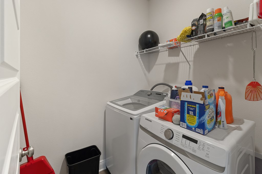 Laundry room with a front-loading dryer, top-loading washer, and wire shelf of cleaning supplies.