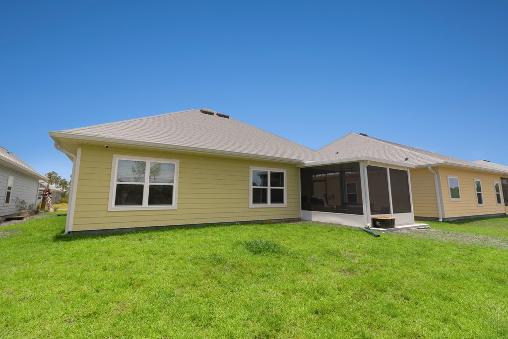 Rear of a yellow-sided home with a screened porch and broad green lawn.