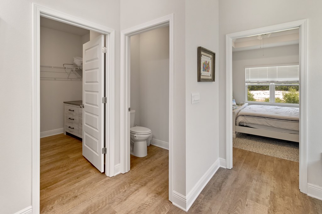 Hallway connecting a closet, toilet room, and bedroom with a wide window.
