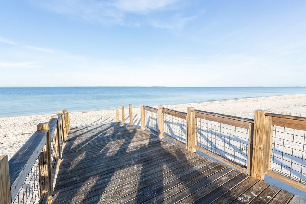 Wooden beach boardwalk opens onto a wide sandy shore and calm blue water.