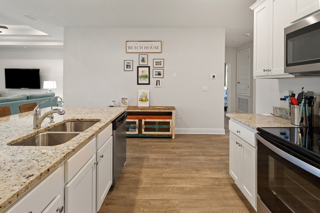 Kitchen with white cabinets, stone counters, stainless appliances, and an open connection to the living area.
