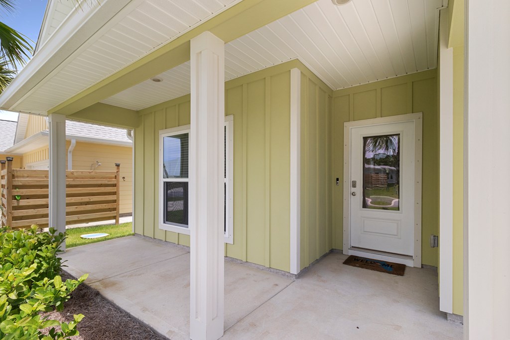 Covered porch with a white front door, yellow siding, and a concrete patio.