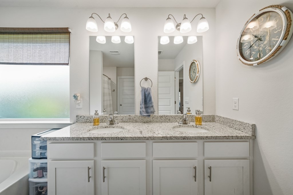 Bathroom with a double-sink granite vanity, matching mirrors, and a frosted window.
