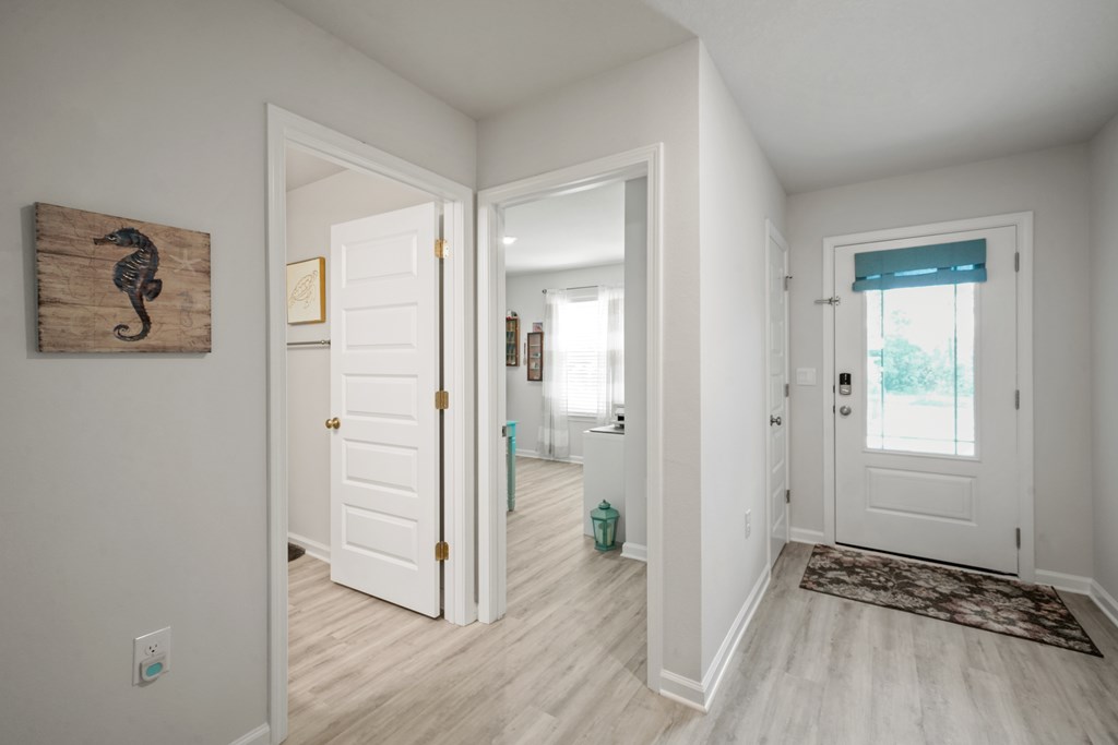 Bright entryway with pale wood floors, a windowed front door, and coastal seahorse wall art.