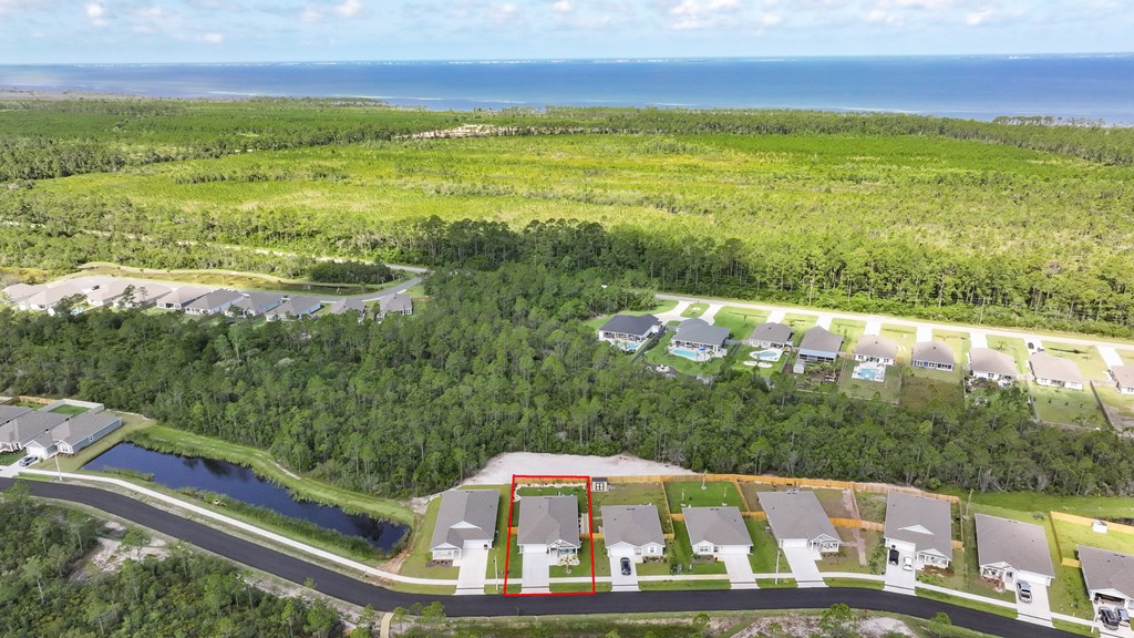 Aerial view of the red-outlined home, with a pond, coastal greenery, and ocean beyond.