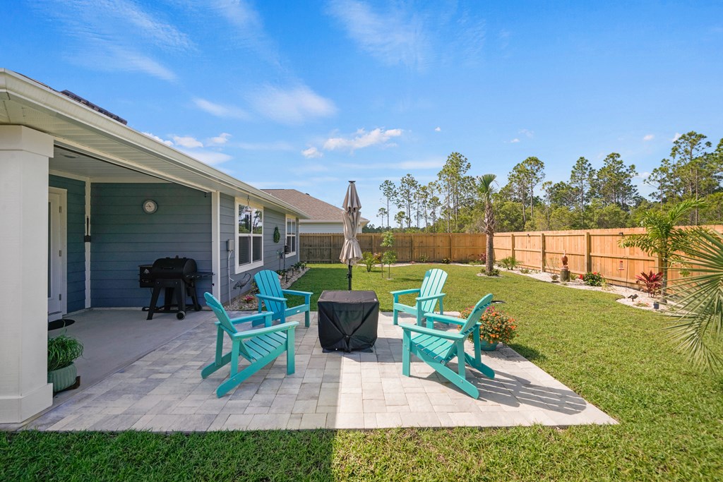 Backyard patio with turquoise Adirondack chairs, a covered table, and a fenced lawn.