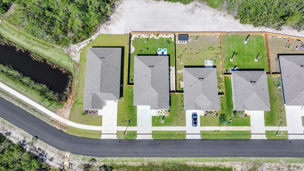 Aerial view of homes along a street beside a narrow pond and wooded area.