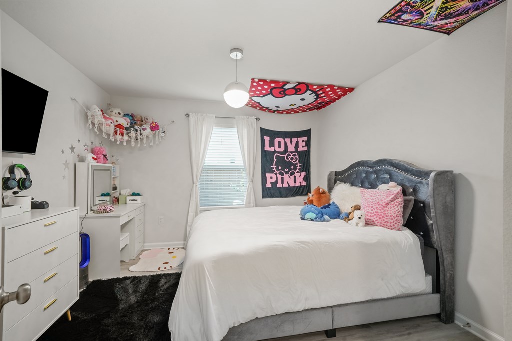 Bedroom with a gray tufted bed, plush toys, and Hello Kitty and LOVE Pink decorations.