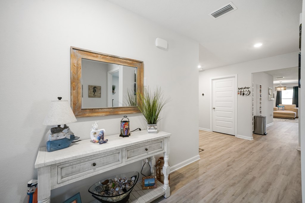 Furnished entry hallway with a rustic-framed mirror above a white console table and a view into the living room.