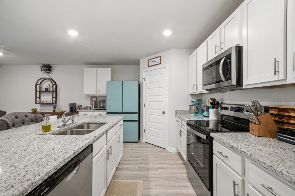 Kitchen with white cabinets, granite counters, a large sink island, and a turquoise refrigerator.