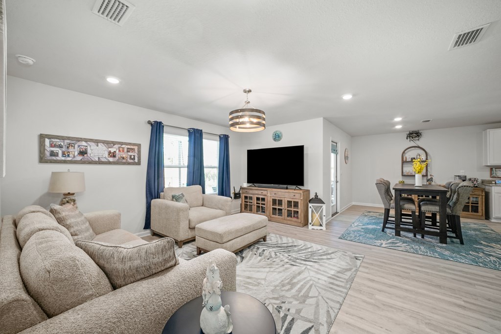 Living room with neutral sofas, blue curtains, and an adjoining dining area.