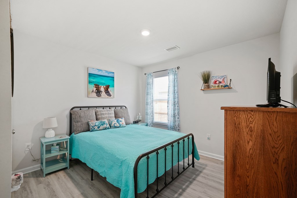 Bedroom with a turquoise quilt, black metal bed, beach art, and blue curtains.