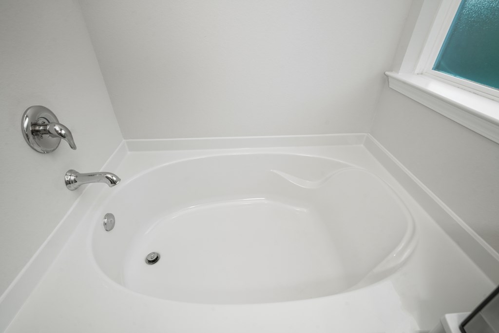 Built-in corner bathtub with chrome fixtures beneath a window.