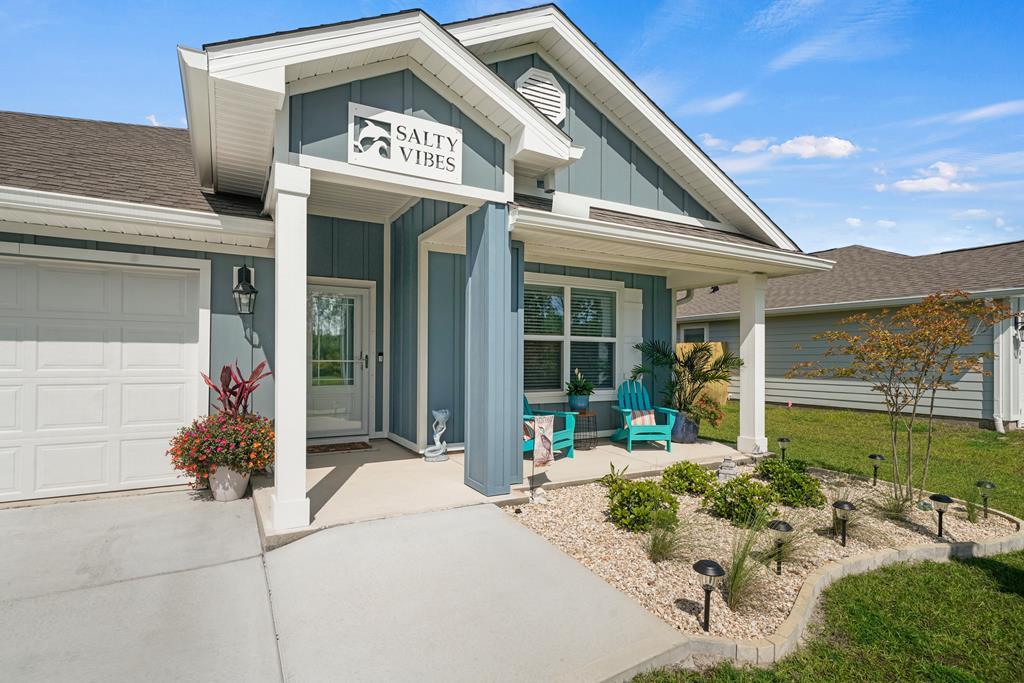 Blue-gray coastal-style home with a covered porch, turquoise chairs, and an attached garage.