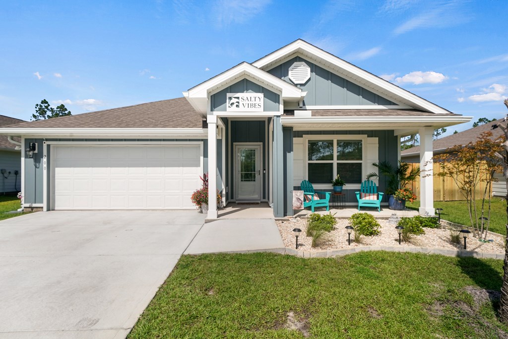 Gray home with a double garage and covered porch furnished with teal chairs.